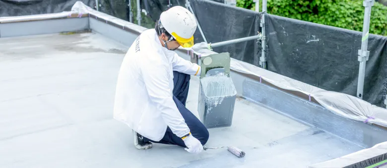 屋上の防水工事を行う職人が防水材を施工している様子