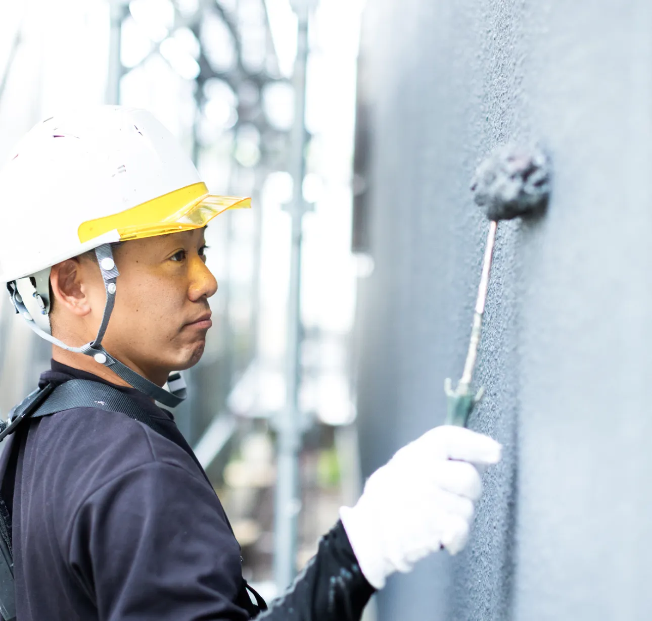 住宅の外壁塗装を行う職人がローラーで外壁を丁寧に塗装している様子