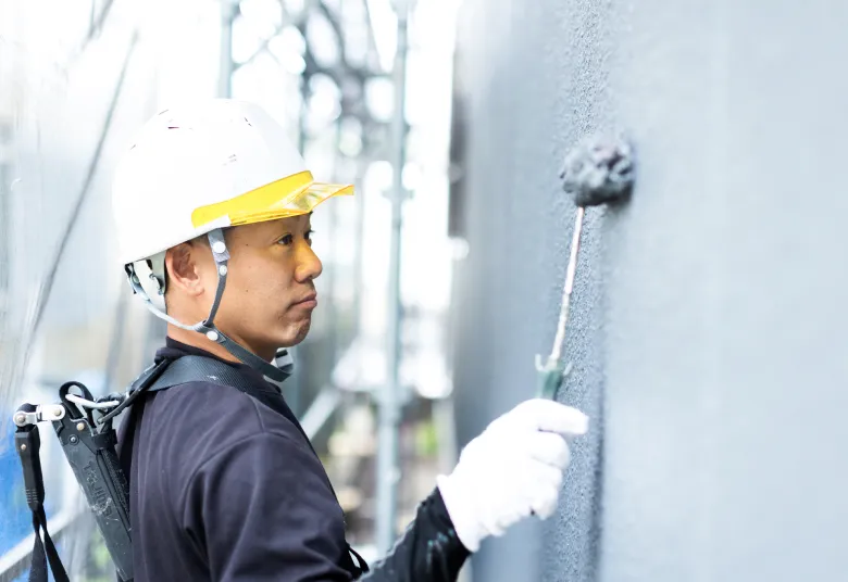 住宅の外壁塗装を行う職人がローラーで外壁を丁寧に塗装している様子
